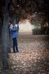 Fototapeta premium slender attractive male musician in blue jacket stands in autumn park alley of fall trees of brown and yellow colours and plays golden old trumpet 