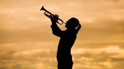 silhouette of a slender trumpeter playing his musical instrument trumpet or horn against background of a yellow sky - obrazy, fototapety, plakaty
