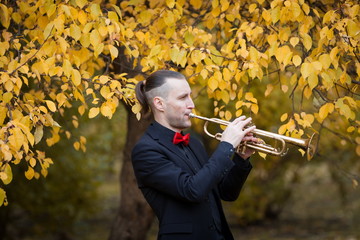 man playing his trumpet in autumn park