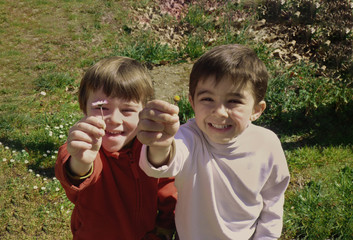 twin children smiling and offering a flower