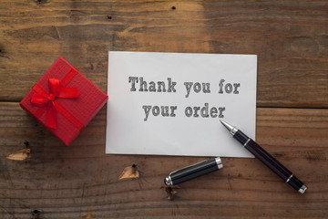 Thank you for your order written on paper with pen,red gift box and wooden background desk.