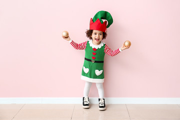 Little girl in costume of elf and with Christmas balls near color wall - obrazy, fototapety, plakaty