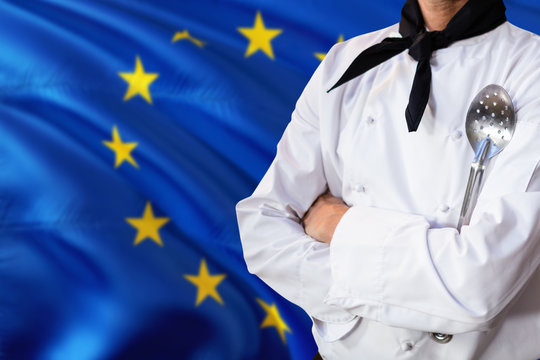 European Union domestic food concept. Professional chef in white uniform is standing with metal spatula. Copy space for text.