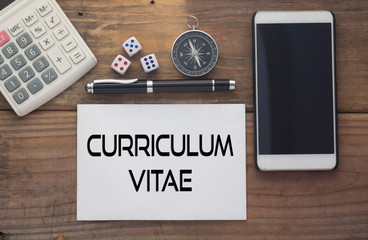 Curriculum Vitae written on paper,Wooden background desk with calculator,dice,compass,smart phone and pen.Top view conceptual.