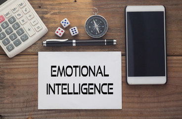 Emotional Intelligence written on paper,Wooden background desk with calculator,dice,compass,smart phone and pen.Top view conceptual.