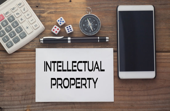 Interlectual Property written on paper,Wooden background desk with calculator,dice,compass,smart phone and pen.Top view conceptual.