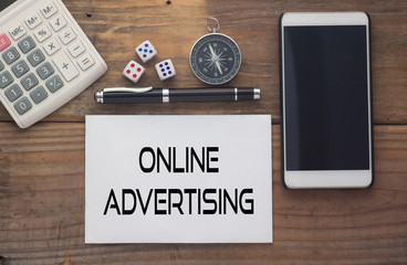Online Advertising written on paper,Wooden background desk with calculator,dice,compass,smart phone and pen.Top view conceptual.