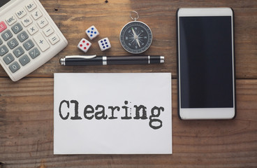 Clearing written on paper,Wooden background desk with calculator,dice,compass,smart phone and pen.Top view conceptual.