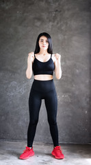 Fototapeta na wymiar The beautiful woman wearing black exercise suit ,raise fists beside her body,doing exercise at home