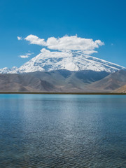 Great cloud covered and snow-capped mountain peak with blue lake water