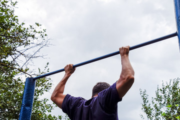 The man pulls himself up on the bar. Playing sports in the fresh