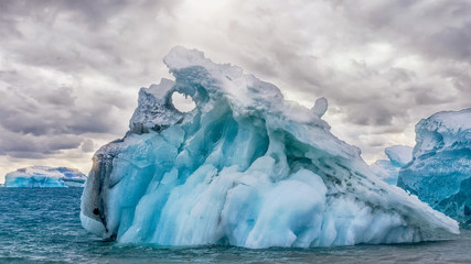 turquoise blue iceberg with small round hole at the top in the Weddell Sea, Antarctica.