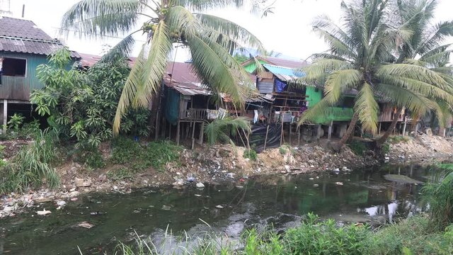 Poverty and pollution. Poor shacks in slum beside water polluted with sewage and plastic garbage 