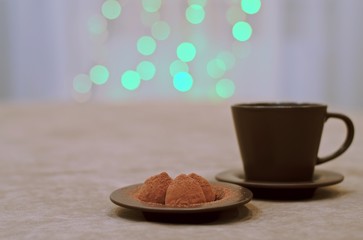  A cup with a saucer and a plate of sweets on the left, against the background of green neon lights in the window.