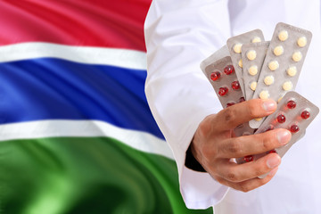 Gambia pharmacy and medicine concept. Doctor holding pills tablet on national flag background. Health theme with copy space for text.