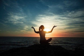 Silhouette of yoga woman meditating on the ocean beach during wonderful sunset.