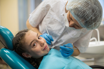 Fototapeta premium Dentist woman doing teeth checkup of little girl looking with fear in a dental chair in medical clinic.
