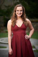 Stunning young Caucasian woman poses in red dress in outdoor courtyard