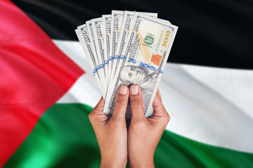 Palestine financial concept. Female hand holding dollar banknotes on national flag background. Currency and money theme with copy space.