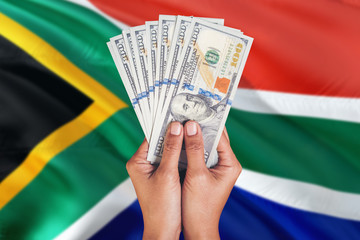 South Africa financial concept. Female hand holding dollar banknotes on national flag background....