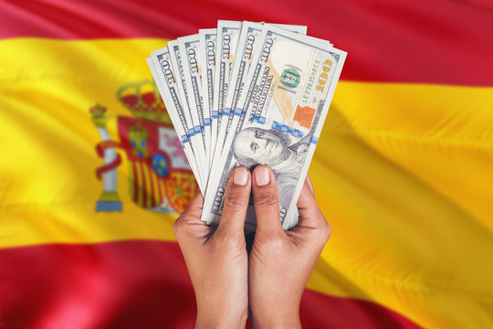 Spain financial concept. Female hand holding dollar banknotes on national flag background. Currency and money theme with copy space.