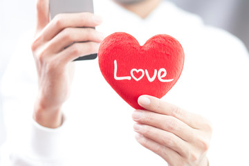 Hand holding red heart with love word and using smartphone 