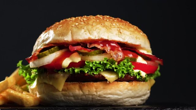 bacon cheeseburger with french fries. Bun with beef meat, cheese, lettuce, tomato, onions, cucumbers, bacon, ketchup and mayonnaise