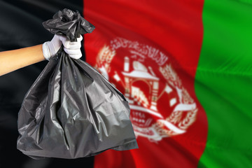 Afghanistan environmental protection concept. The male hand holding a garbage bag on national flag background. Ecological and recycling theme with copy space.
