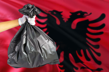 Albania environmental protection concept. The male hand holding a garbage bag on national flag background. Ecological and recycling theme with copy space.