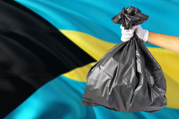 Bahamas environmental protection concept. The male hand holding a garbage bag on national flag background. Ecological and recycling theme with copy space.