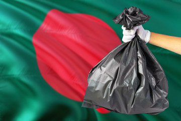 Bangladesh environmental protection concept. The male hand holding a garbage bag on national flag background. Ecological and recycling theme with copy space.