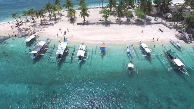 Areal camera drone hover over clear shallow coastal blue waters off shore of white sand beach on luxury tropical resort island in the summer vacation season