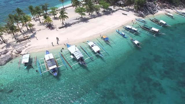 Sloping underwater sand bank extending from white sand beach at sea level island with docked boats, showing coconut banana and lush planted palm trees and underwater rocks