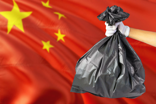 China environmental protection concept. The male hand holding a garbage bag on national flag background. Ecological and recycling theme with copy space.