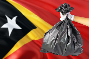 East Timor environmental protection concept. The male hand holding a garbage bag on national flag background. Ecological and recycling theme with copy space.