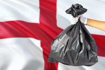England environmental protection concept. The male hand holding a garbage bag on national flag background. Ecological and recycling theme with copy space.