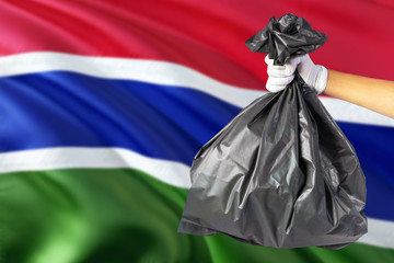 Gambia environmental protection concept. The male hand holding a garbage bag on national flag background. Ecological and recycling theme with copy space.