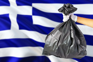 Greece environmental protection concept. The male hand holding a garbage bag on national flag background. Ecological and recycling theme with copy space.