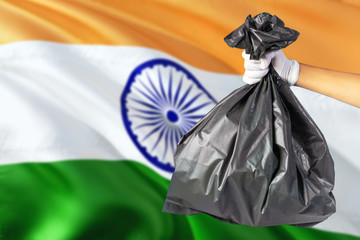 India environmental protection concept. The male hand holding a garbage bag on national flag background. Ecological and recycling theme with copy space.