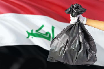 Iraq environmental protection concept. The male hand holding a garbage bag on national flag background. Ecological and recycling theme with copy space.