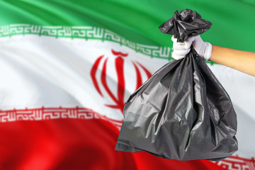 Iran environmental protection concept. The male hand holding a garbage bag on national flag background. Ecological and recycling theme with copy space.
