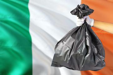 Ireland environmental protection concept. The male hand holding a garbage bag on national flag background. Ecological and recycling theme with copy space.
