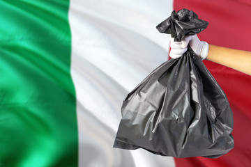 Italy environmental protection concept. The male hand holding a garbage bag on national flag background. Ecological and recycling theme with copy space.