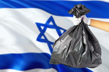 Israel environmental protection concept. The male hand holding a garbage bag on national flag background. Ecological and recycling theme with copy space.