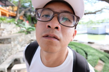 Selective focus tourist young handsome asian man wear eye glasses white shirt and hat with braces and looking at camera,Portrait of a smiling athletic young Asian man  an early morning,blurred and so