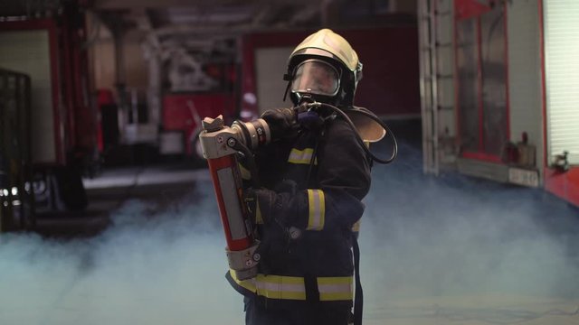 female firefighter portrait wearing full equipment, oxygen mask, and emergency rescue equipment, hard tool, smoke and fire trucks in the background. 