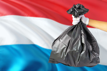 Luxembourg environmental protection concept. The male hand holding a garbage bag on national flag background. Ecological and recycling theme with copy space.