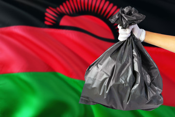 Malawi environmental protection concept. The male hand holding a garbage bag on national flag background. Ecological and recycling theme with copy space.