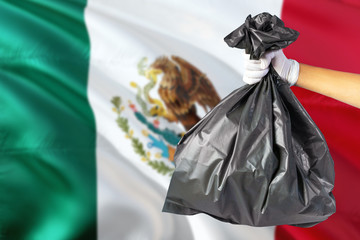 Mexico environmental protection concept. The male hand holding a garbage bag on national flag background. Ecological and recycling theme with copy space.