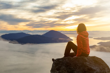 Adventurous Caucasian Girl sitting on top of a mountain during a colorful winter sunset. Taken on...